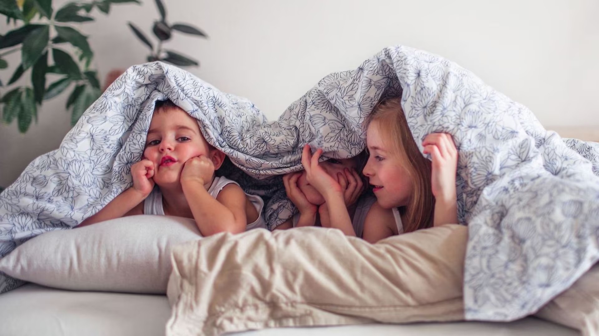 3 Kinder gucken unter einer Decke hervor