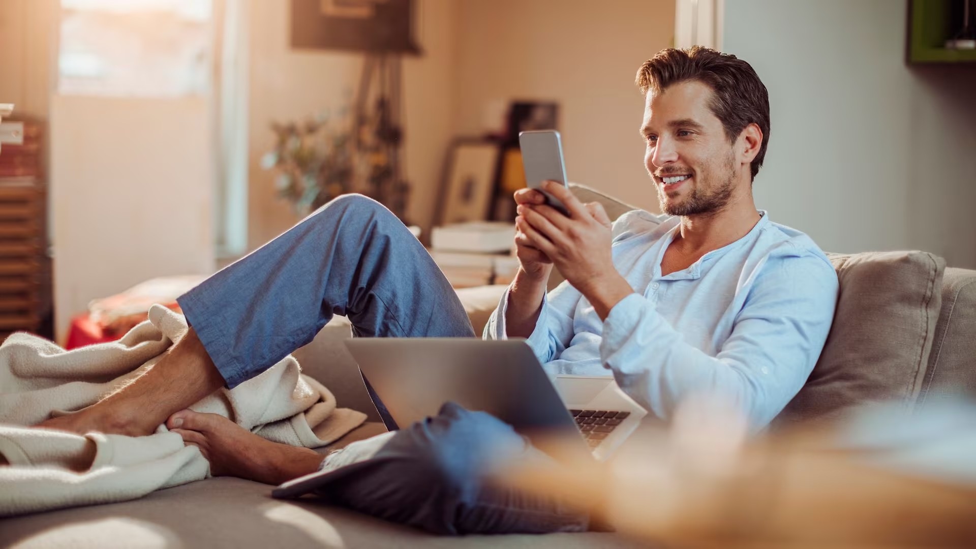 Mann auf einer Couch mit Handy und Laptop